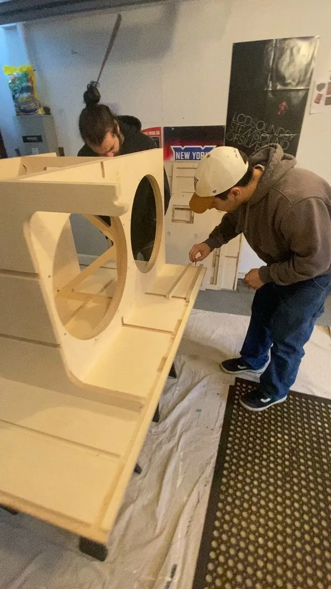 Two crew members fitting panels on a raw birch cabinet