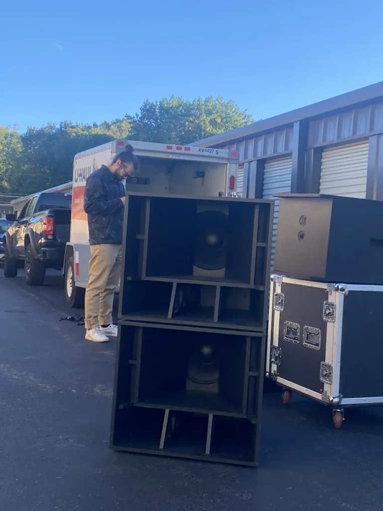 Two stacked subwoofers next to a road case and moving truck